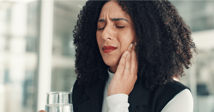 A woman holding her jaw in pain, illustrating common symptoms of TMJ disorders like facial discomfort or teeth grinding.
