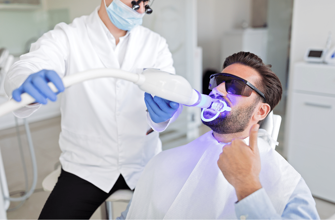A patient in protective eyewear receiving an in-office teeth whitening treatment in Sacramento, featuring a specialized blue light to accelerate the bleaching process.