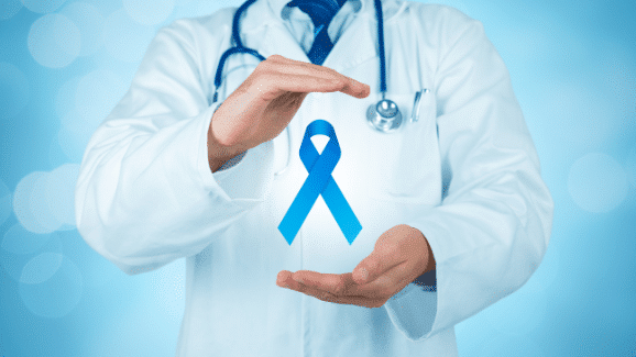 A medical professional in a white coat and stethoscope holding a blue awareness ribbon, representing the importance of oral cancer screening in Sacramento.