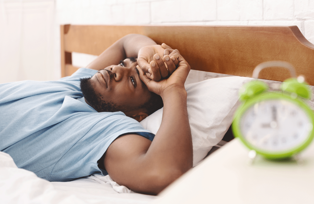 A man lying in bed looking awake and frustrated, representing common sleep apnea symptoms like daytime drowsiness and restless sleep.