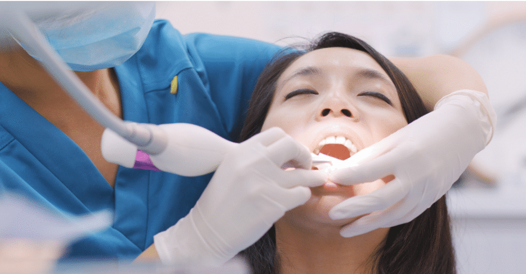 A female patient lying back in a dental chair receiving a deep cleaning treatment from a dental professional using specialized ultrasonic tools.