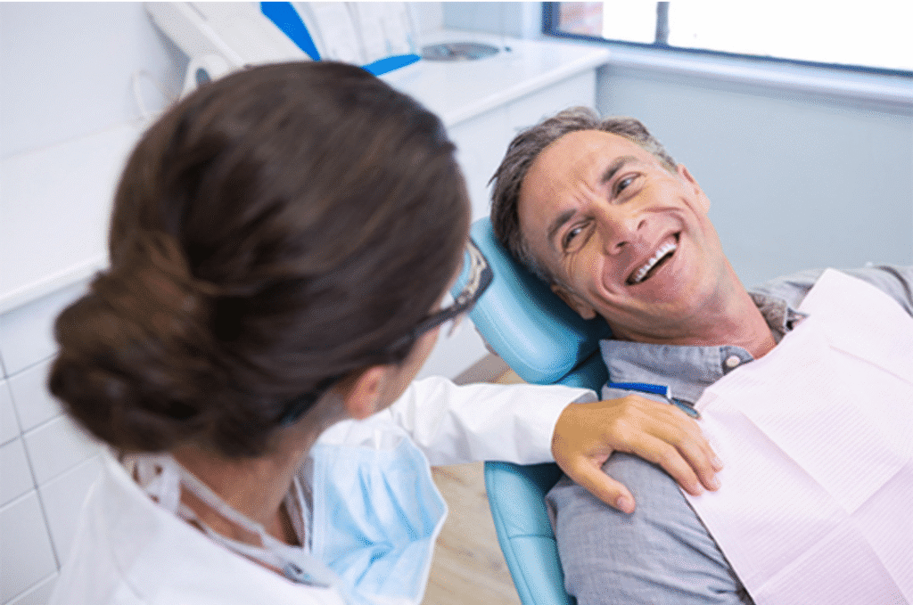 A happy adult male patient in a dental chair smiling at a female dentist during a full mouth reconstruction consultation.